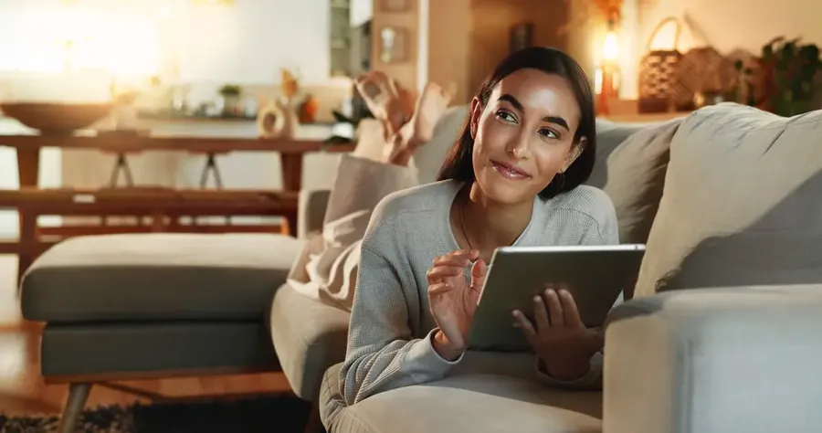 Smile tablet and thinking with woman on sofa in living room of home for purchase decision Ecommerce online shopping and technology with happy person in apartment for budget choice or option